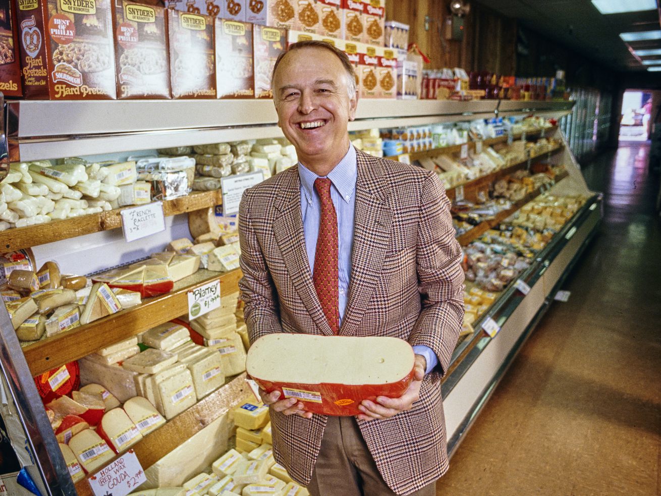 Joe Coulombe, founder of Trader Joe's, holding a wheel of cheese in one of his stores
